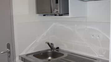 A compact kitchen with a microwave, sink, and a small refrigerator.