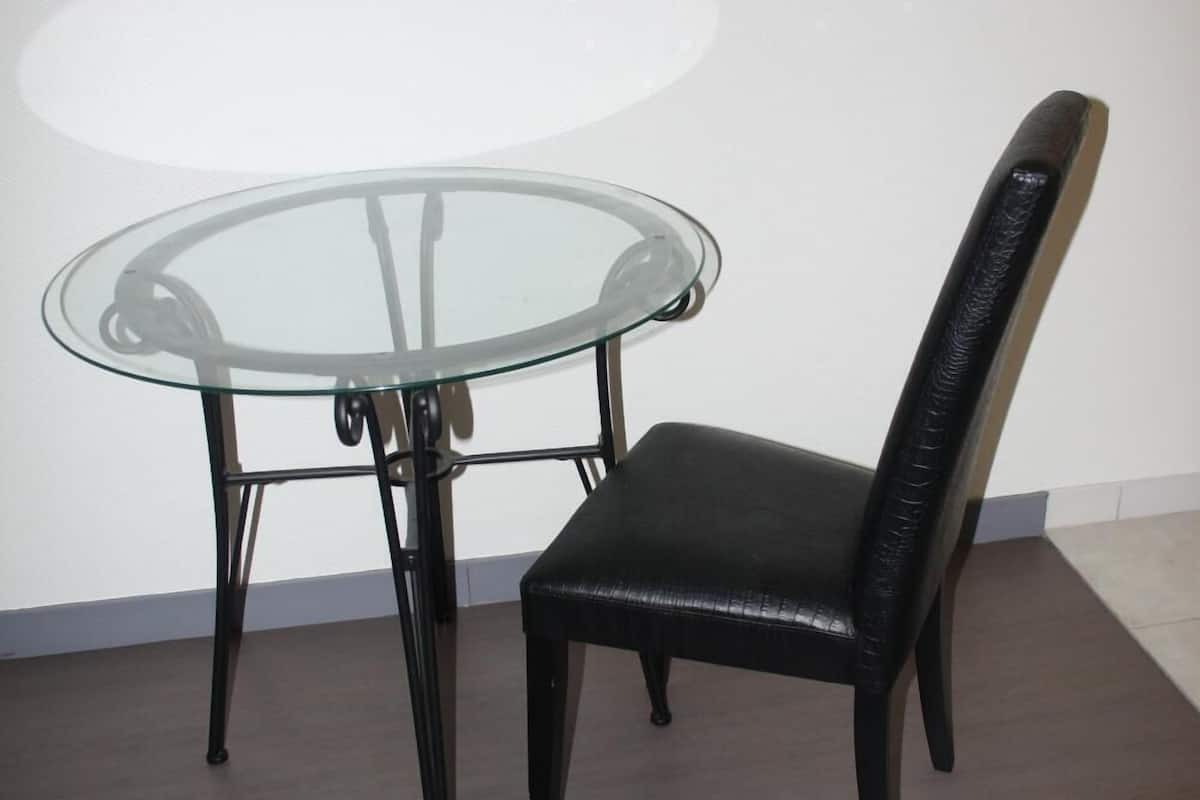 A glass-top table with a black metal frame and a black leather chair with a high backrest.