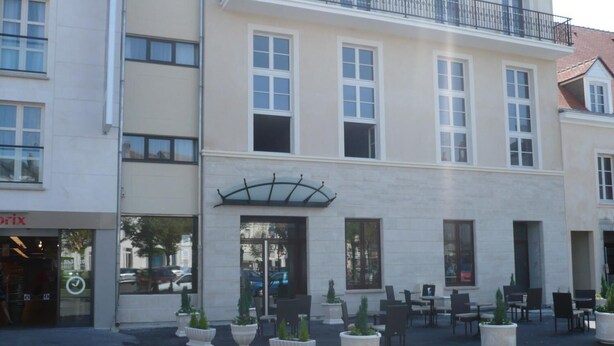 A building with a cafe area featuring outdoor seating and potted plants. - Résidence d'Artagnan (Montargis)