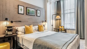 A hotel room with a large bed, two bedside tables with lamps, a small table with a chair, and a view of the outdoors through a window. - The Princes Square Hotel (London)