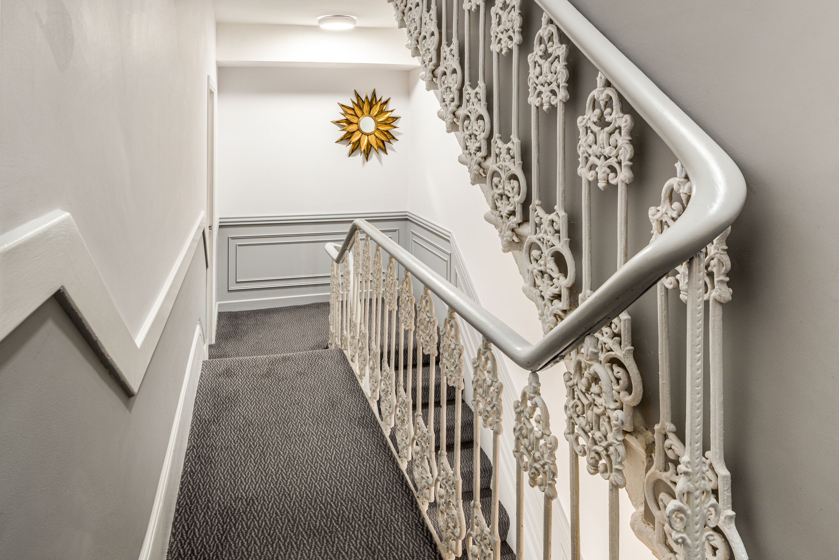 Una escalera con barandales blancos decorados y un suelo de moqueta con textura.