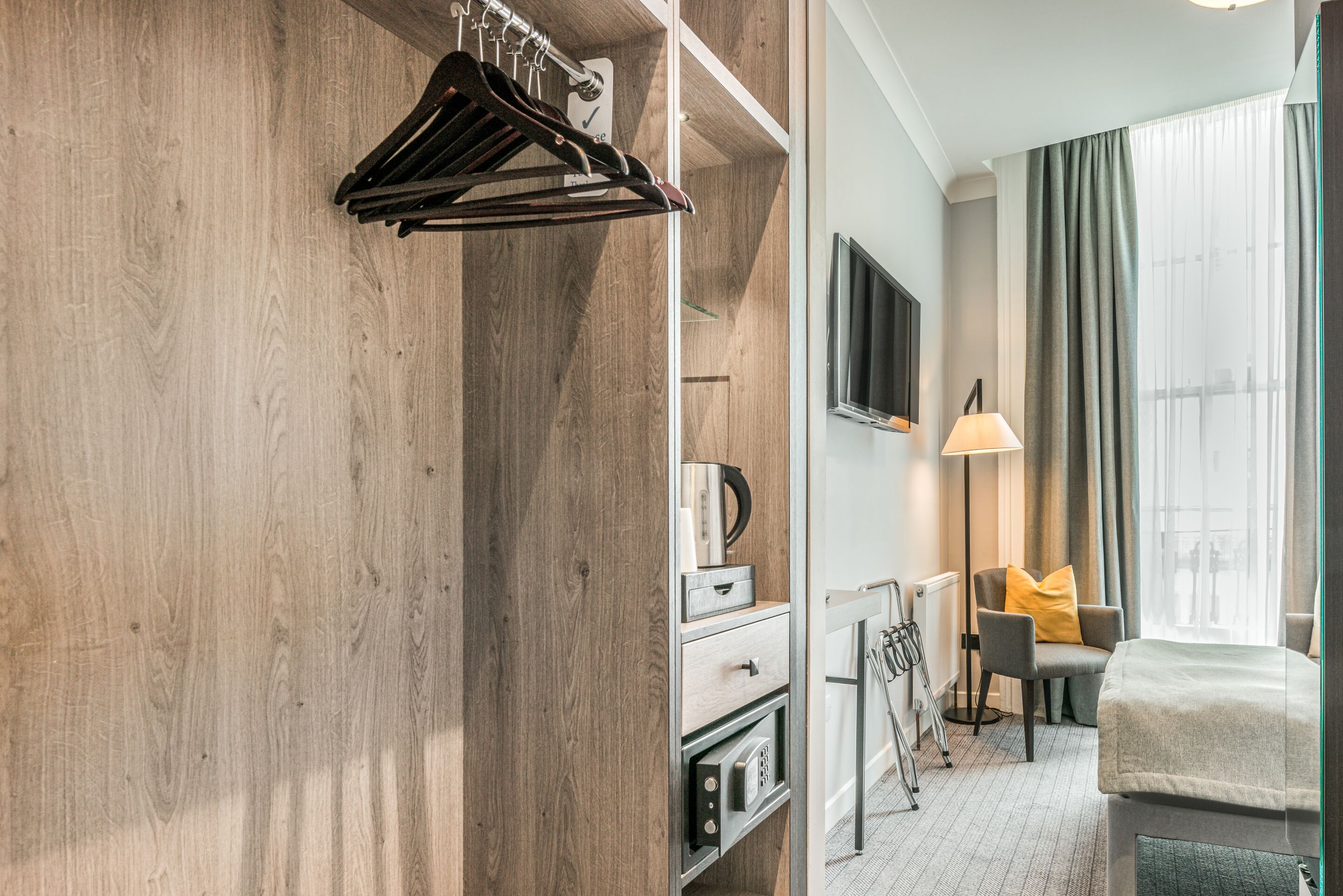 Une chambre d’hôtel avec une armoire en bois, un lit, un bureau avec une lampe et une chaise avec un coussin.