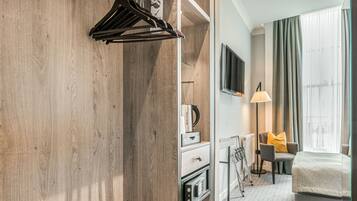 Une chambre d’hôtel avec une armoire en bois, un lit, un bureau avec une lampe et une chaise avec un coussin.