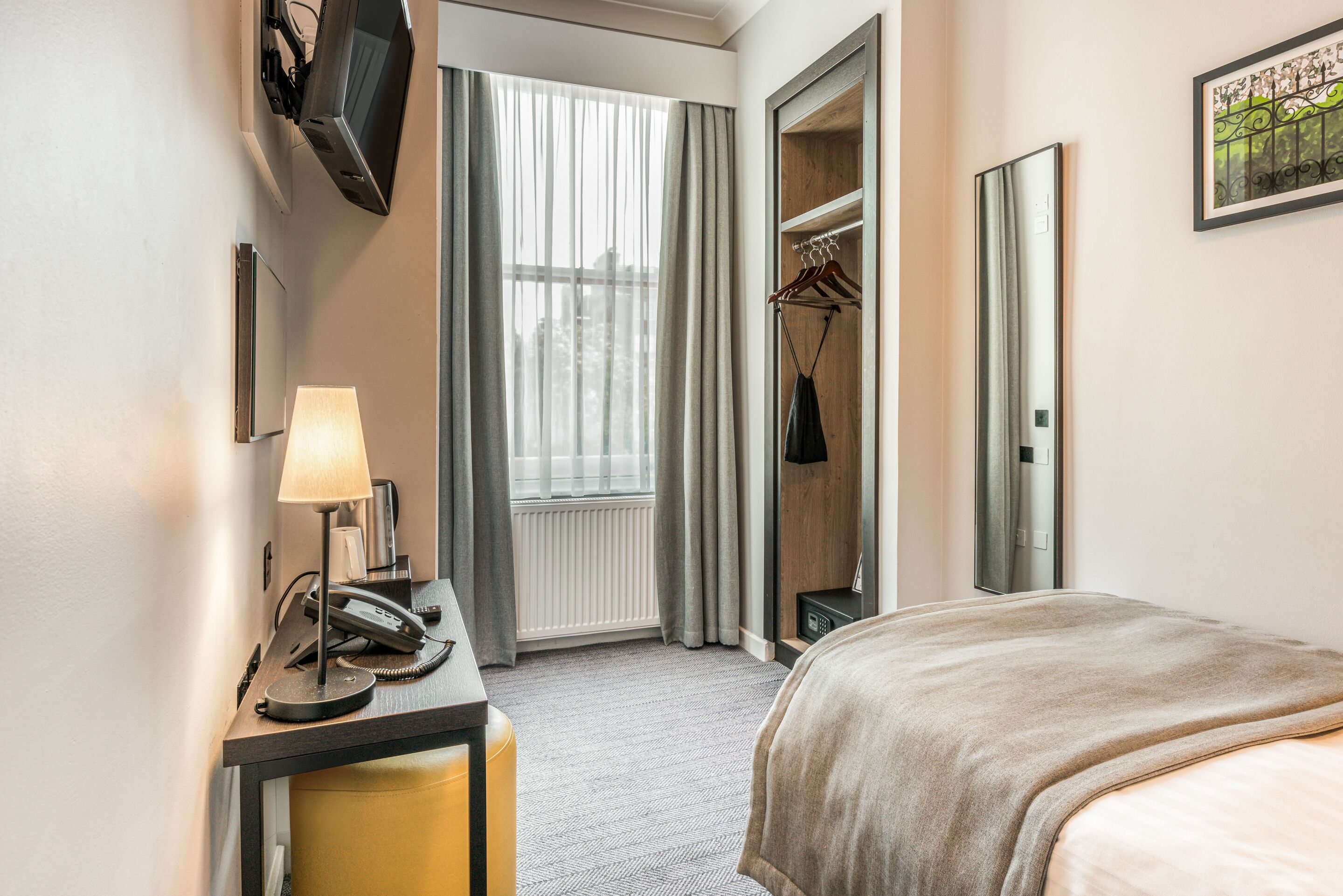 Une chambre d’hôtel comprenant un lit, un bureau avec une lampe, un téléphone, un porte-manteau et une armoire.