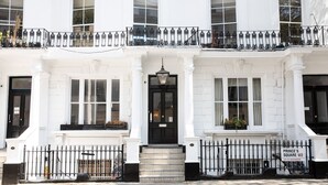 A white townhouse with a black front door, a small balcony with black iron railings, and a sign indicating "Prince's Square W2". - The Princes Square Hotel (London)