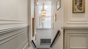 A staircase with white walls, a chandelier, and framed pictures. - The Princes Square Hotel (London)