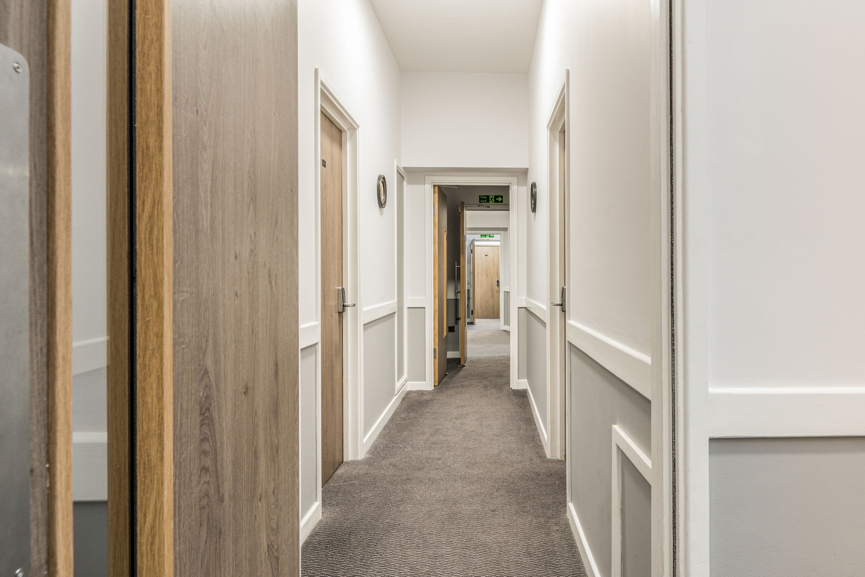 A hallway with wooden doors and white walls, leading to a room with a carpeted floor.