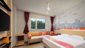 A hotel room with a bed, a sofa, a TV, a ceiling fan, a window with curtains, and a cityscape wall mural. - Ginger Noida Sector 63 (Noida)
