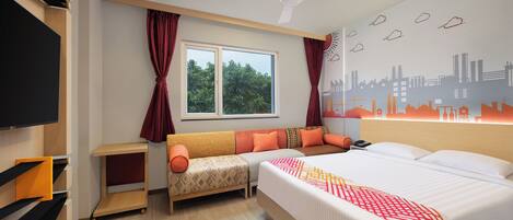 A hotel room with a bed, a sofa, a TV, a ceiling fan, a window with curtains, and a cityscape wall mural.