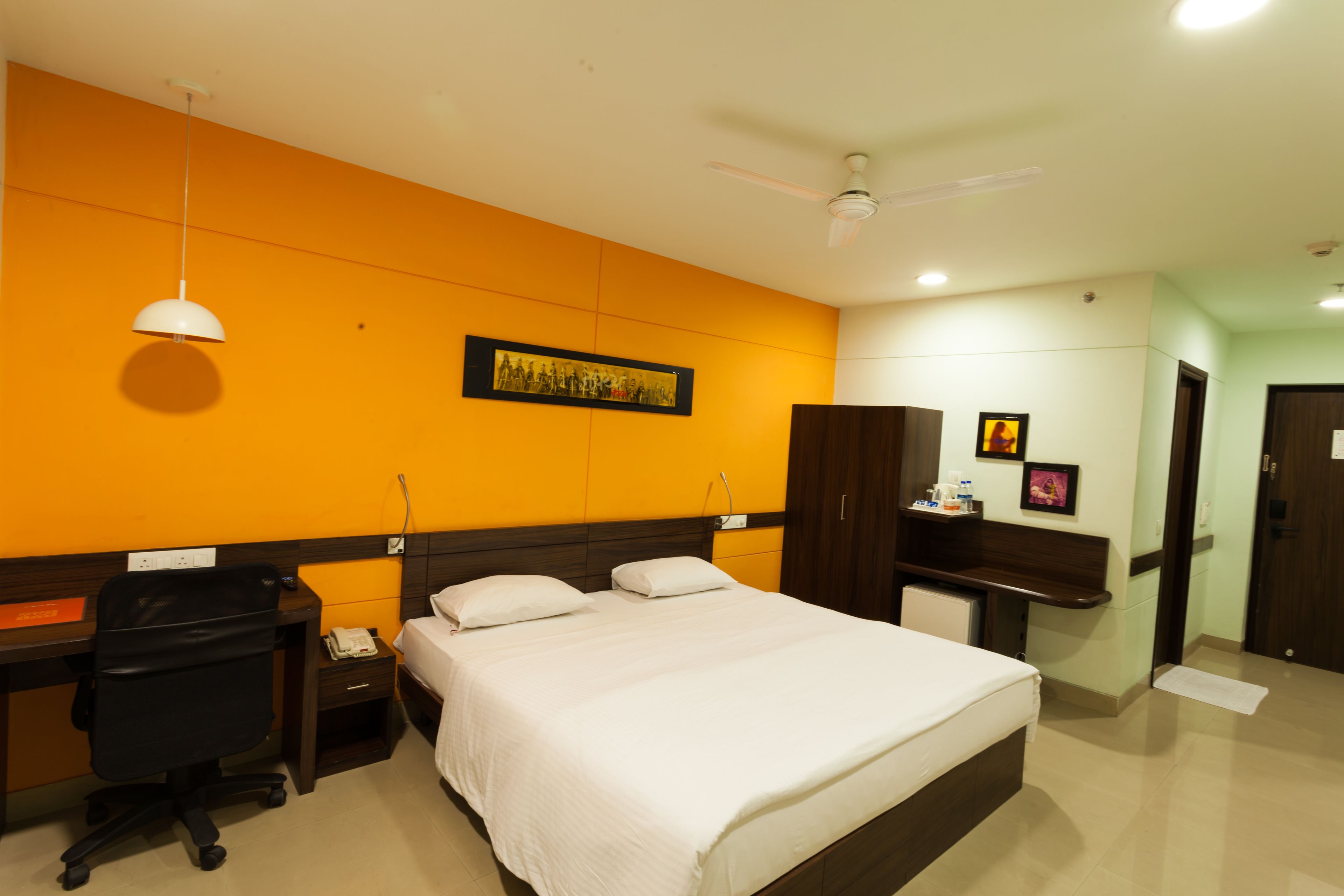 A hotel room with a bed, desk, chair, wardrobe, and ceiling fan.