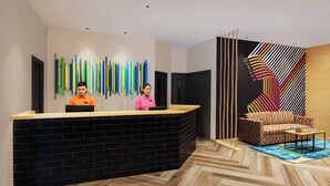 A reception area with a black brick counter, colorful vertical light fixtures, a patterned sofa, and a herringbone wood floor. - Ginger Noida Sector 63 (Noida)