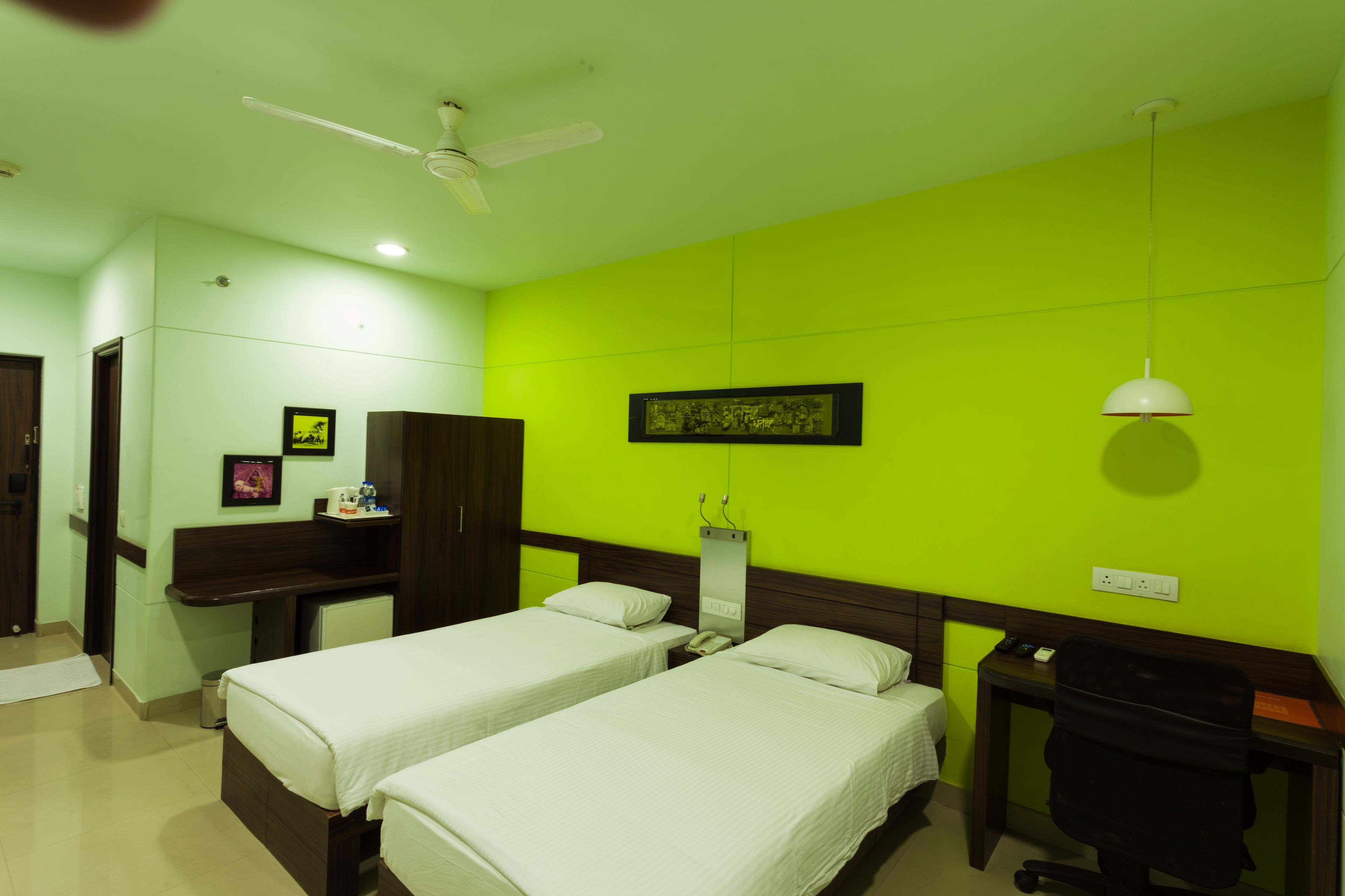 A hotel room with two beds, a desk, a chair, a ceiling fan, and a wall-mounted telephone.