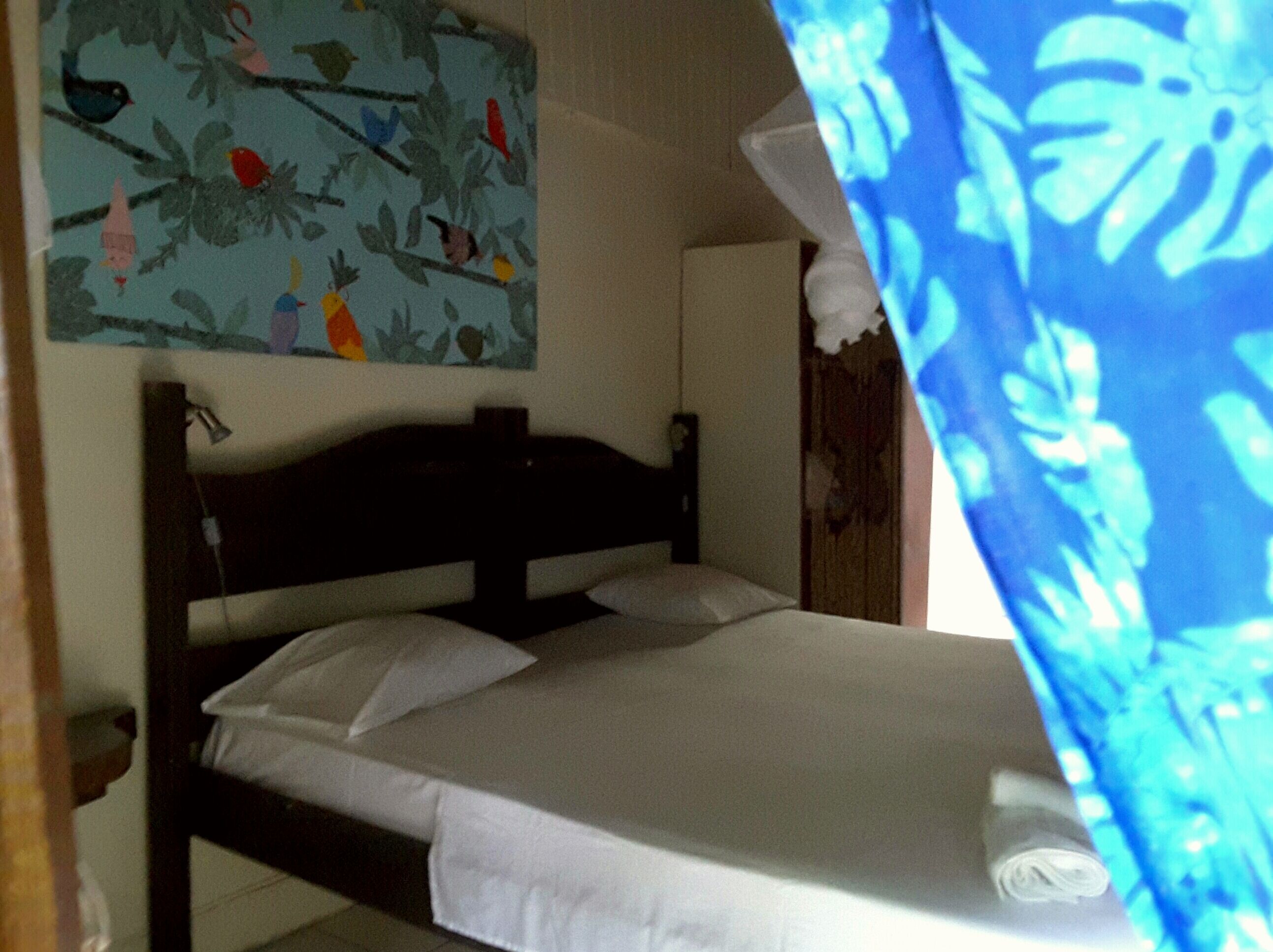 Un lit avec du linge de lit blanc, une tête de lit et un tableau représentant des oiseaux accroché au mur au-dessus.