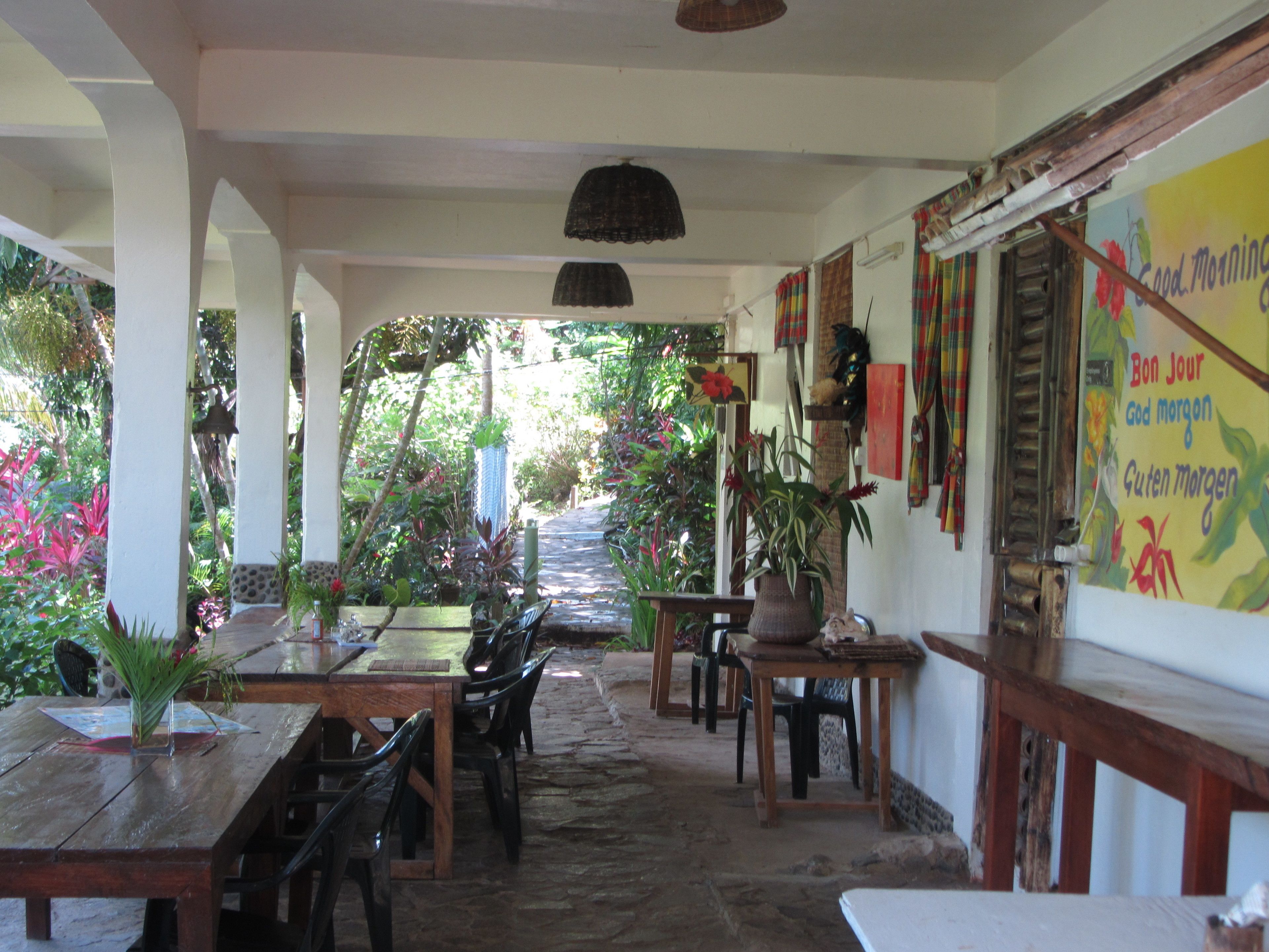 An outdoor dining area with wooden tables and chairs, surrounded by lush greenery and potted plants.
