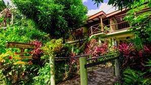 A lush garden leading to a wooden structure with a sign indicating amenities like an office, nature bungalows, and a restaurant.