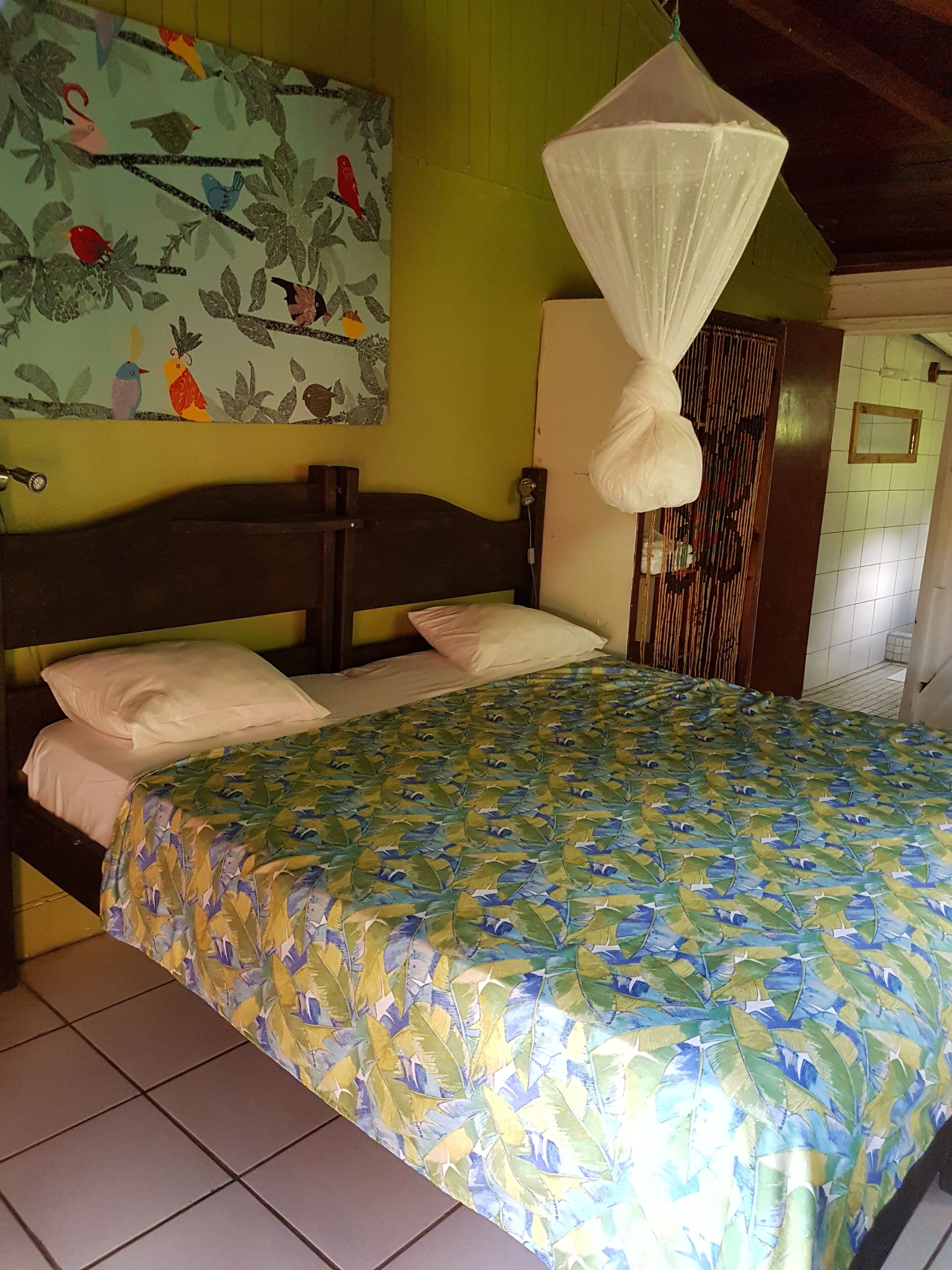 A bed with a leaf-patterned bedspread, a wooden headboard, and a wall with a bird-themed painting.