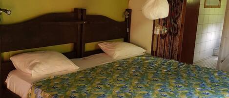 A bed with a leaf-patterned bedspread, a wooden headboard, and a wall with a bird-themed painting.