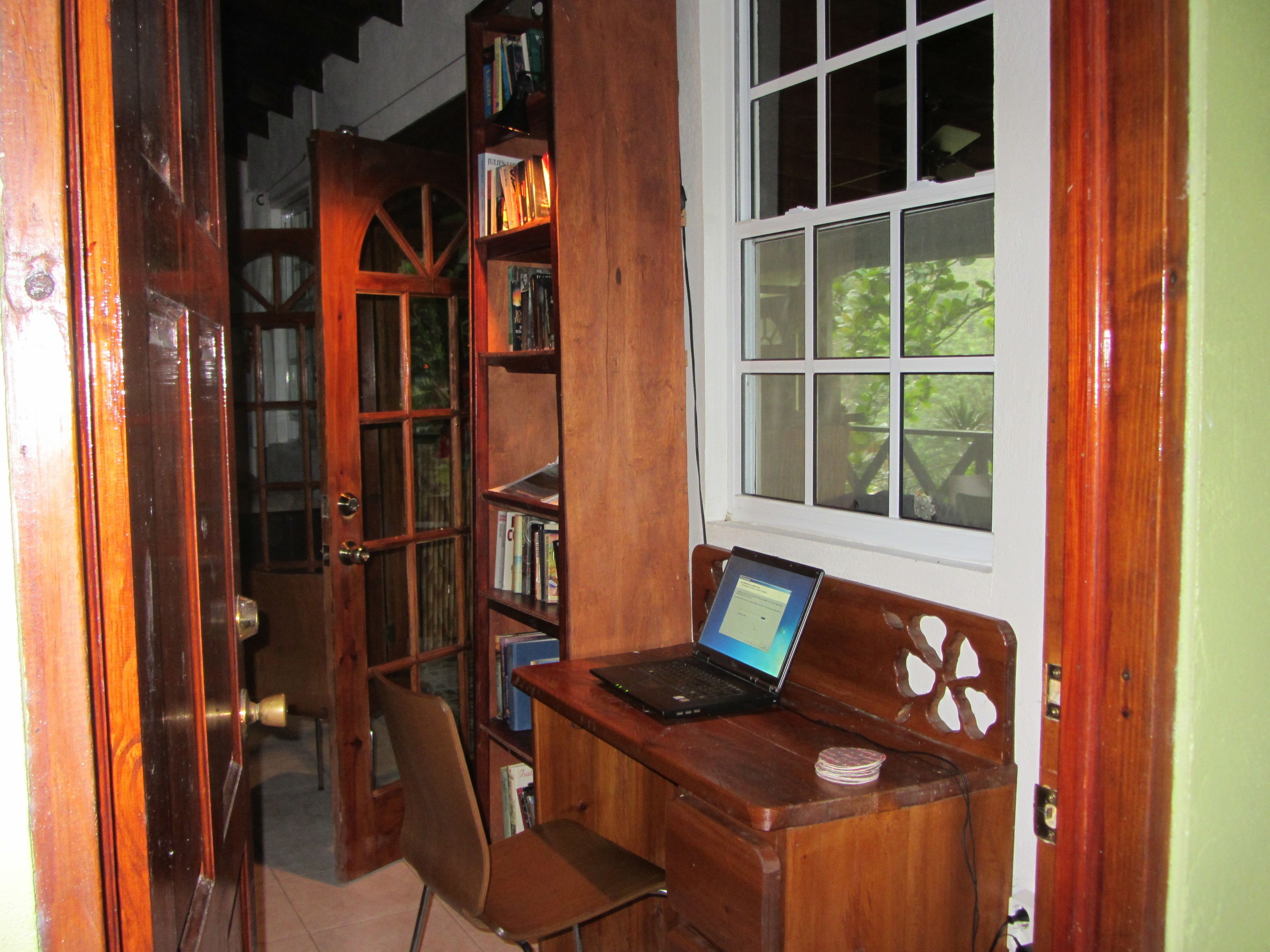 Un bureau en bois avec un ordinateur portable, une chaise et une bibliothèque, dans une pièce avec une fenêtre.