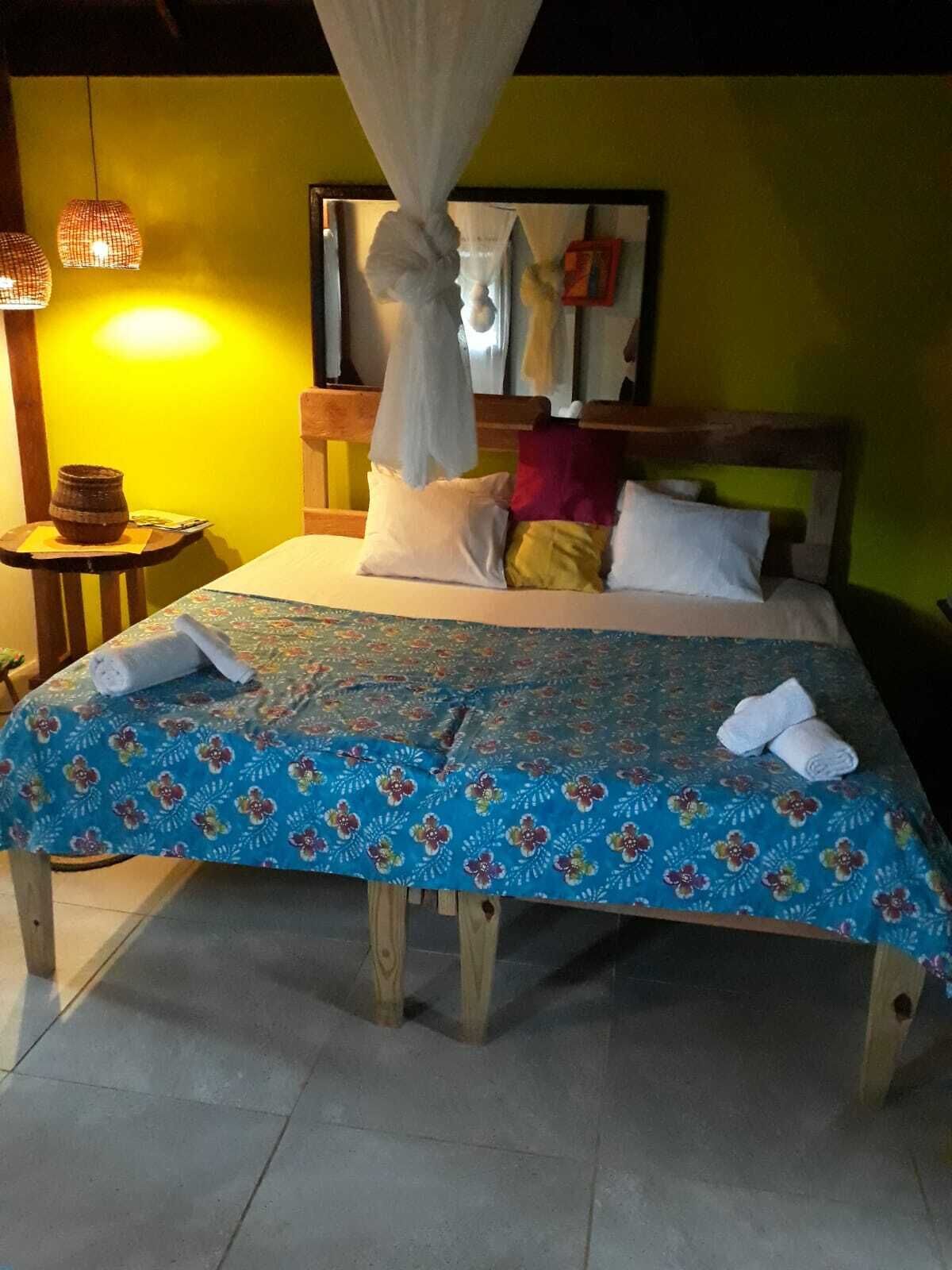 A bed with a canopy, a small table with a basket, and a wall-mounted shelf with towels.