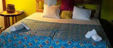 A bed with a canopy, a small table with a basket, and a wall-mounted shelf with towels.