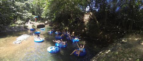 Personas flotando en balsas azules en un río rodeado de árboles.