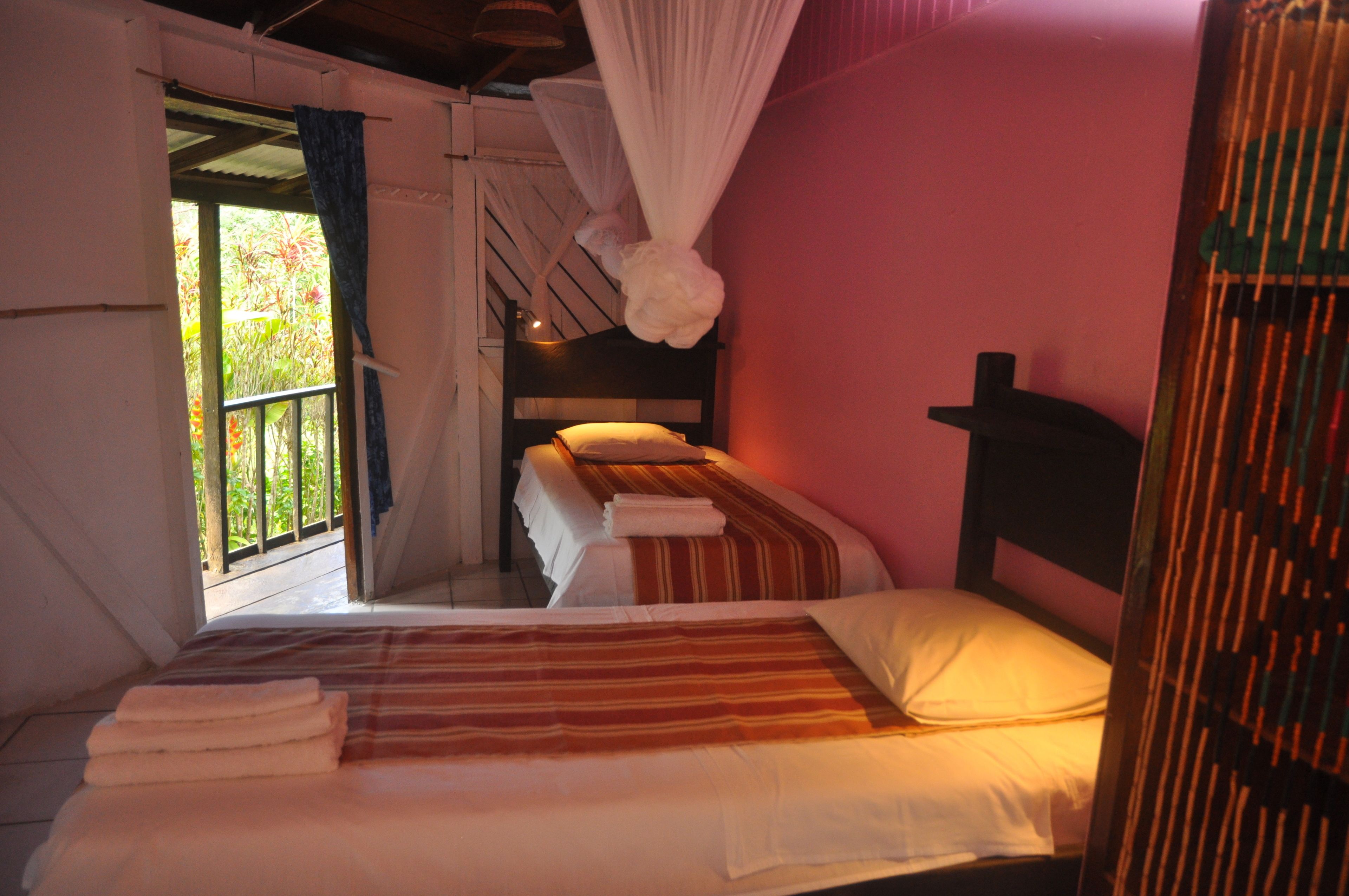 A bedroom with two beds, a window with curtains, and a mosquito net.