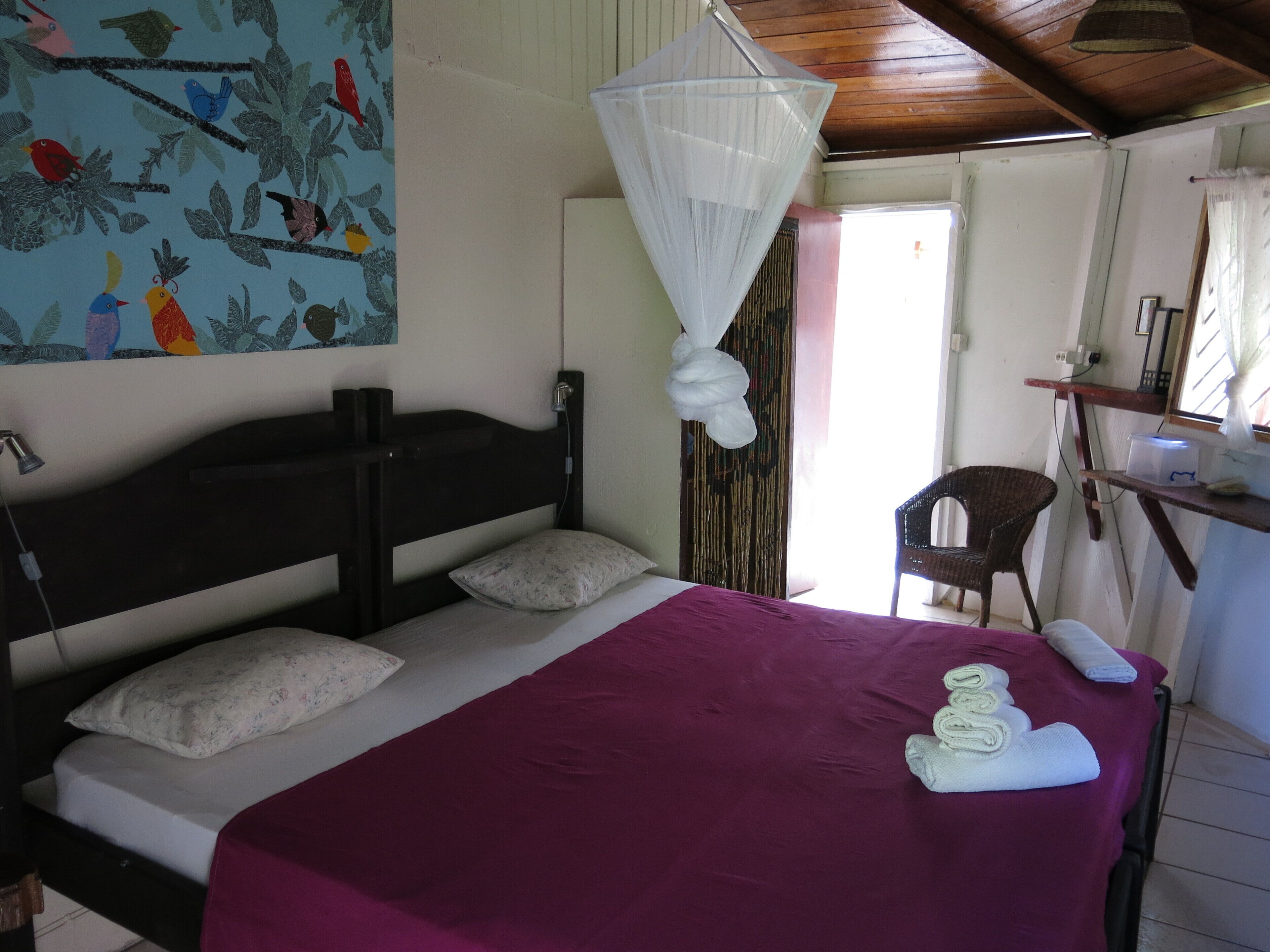 A bedroom with a bed, a mosquito net, a chair, and a shelf with items.