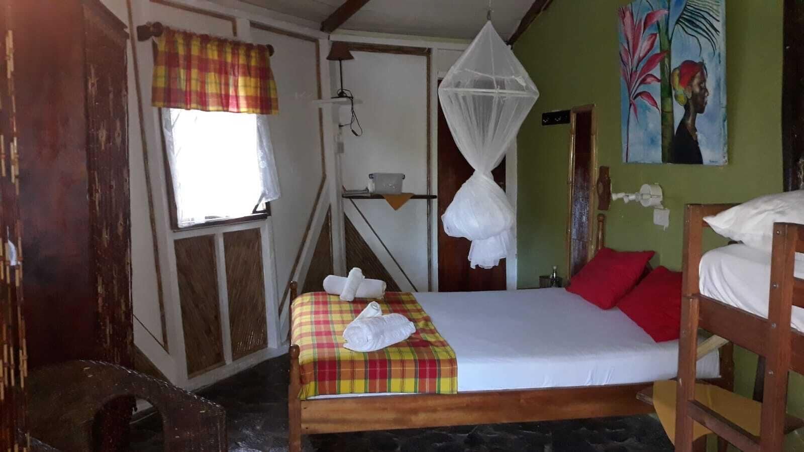 Una habitació amb un llit, una finestra amb cortina escocesa, una mosquitera i un quadre a la paret.