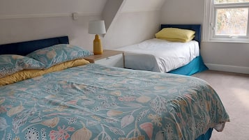 A bedroom with a large bed, a smaller bed, a nightstand, a lamp, and a window with a view of trees.