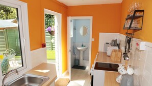 A compact kitchen with a sink, a countertop, a microwave, and a shelf with glassware. - Abbey View Holiday Flats (Torquay)