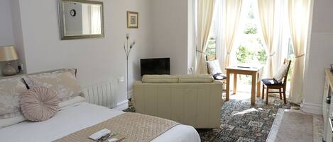 A hotel room with a bed, a sofa, a TV, a table, and a chair.