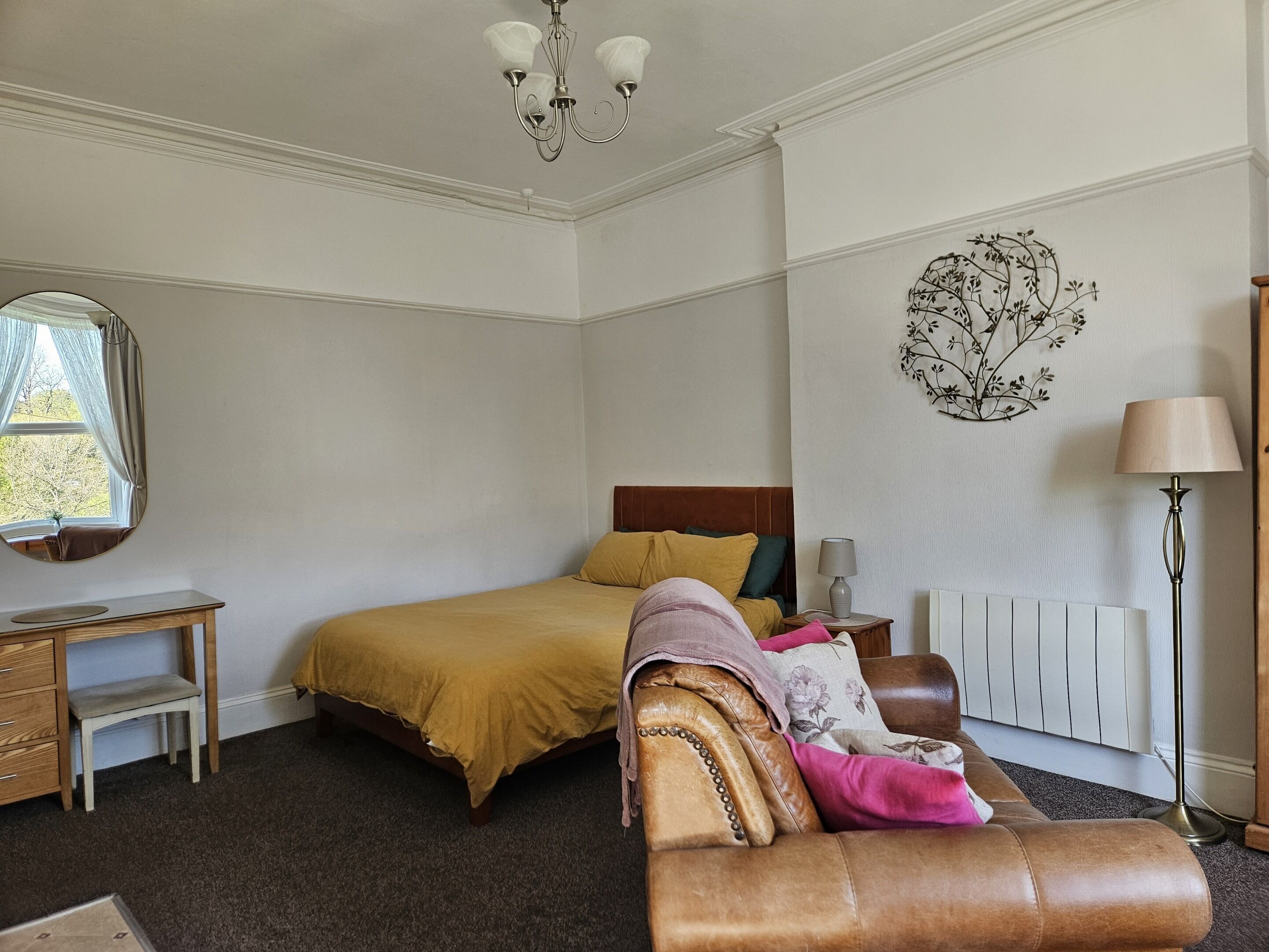 A bedroom with a bed, a desk, a chair, a radiator, and a lamp.