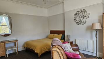 A bedroom with a bed, a desk, a chair, a radiator, and a lamp.