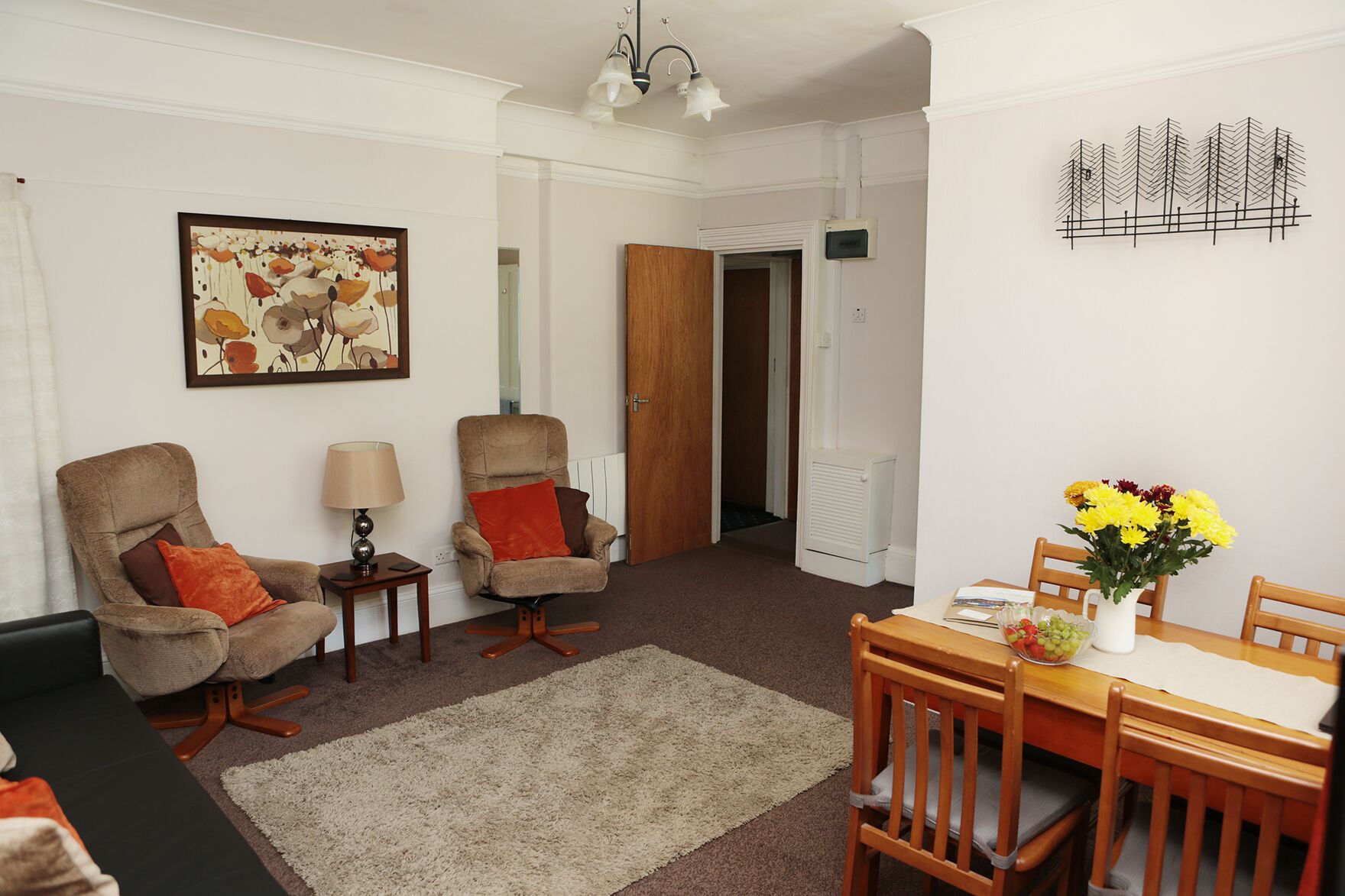 A living room with two armchairs, a table with a vase of flowers, and a painting on the wall.
