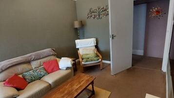 Una sala de estar con un sofá, una mesa de centro de madera, una lámpara y un adorno en la pared.