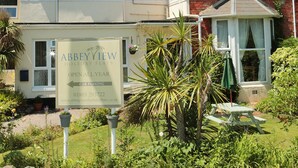 A two-story brick building with a sign indicating it is a holiday flat. - Abbey View Holiday Flats (Torquay)