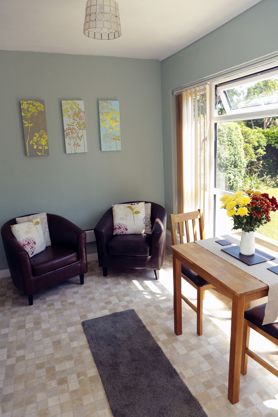 A living room with two leather armchairs, a wooden dining table, and a large window with a view of greenery.