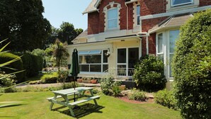 A two-story house with a garden patio, a conservatory, and a large lawn. - Abbey View Holiday Flats (Torquay)