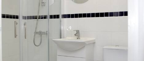 Un baño moderno con cabina de ducha de vidrio, un lavabo blanco, un inodoro y un espejo sobre el lavabo.