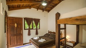 A wooden-framed bed with a headboard, a wooden bench, and a small table with a lamp. - Indra Inn (Cabo Velas)