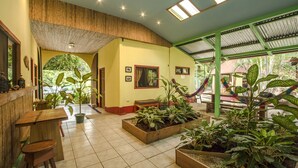 A spacious indoor area with wooden furniture, potted plants, and a tiled floor. - Indra Inn (Cabo Velas)