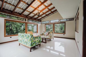 A spacious room with large windows, wooden beams, and two floral-patterned sofas.