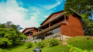 A wooden cabin with a balcony, surrounded by lush greenery and flowers.