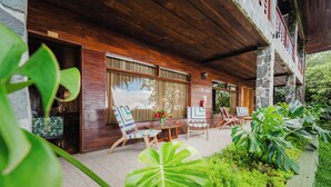A wooden exterior with a stone pillar, a covered patio with two chairs and a table, and a large window.