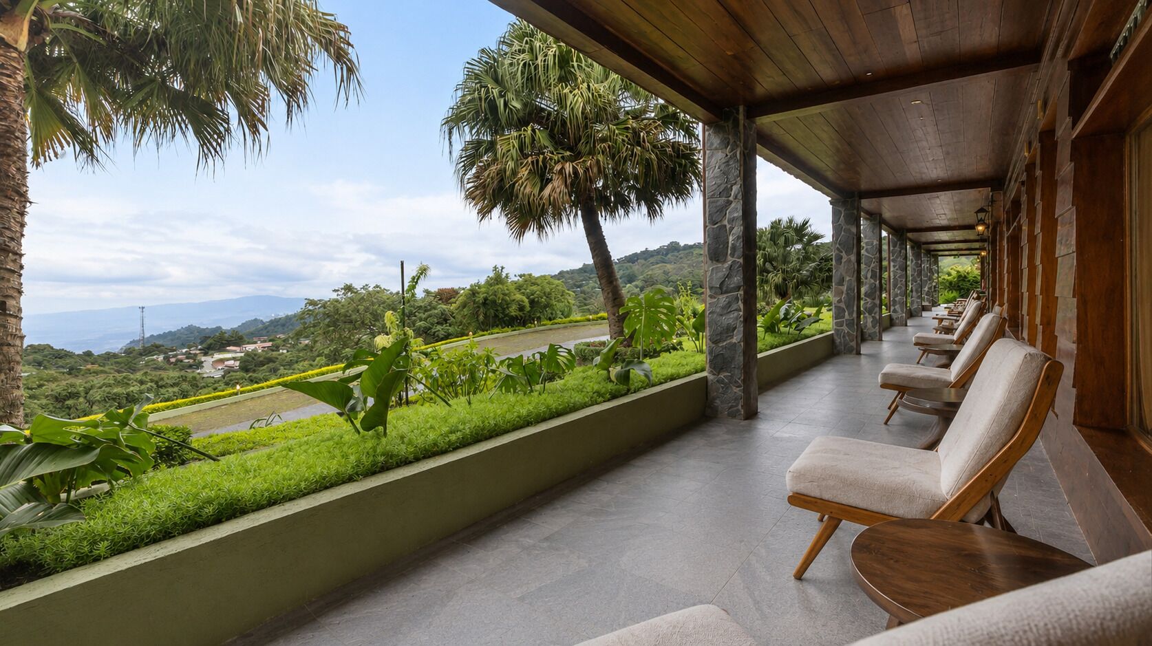A covered outdoor seating area with chairs and a view of a landscaped garden and distant landscape.