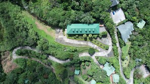 An aerial view of a property with a central building surrounded by a winding road, multiple parking areas, and lush greenery. - Hotel Heliconia - Monteverde (Monteverde)