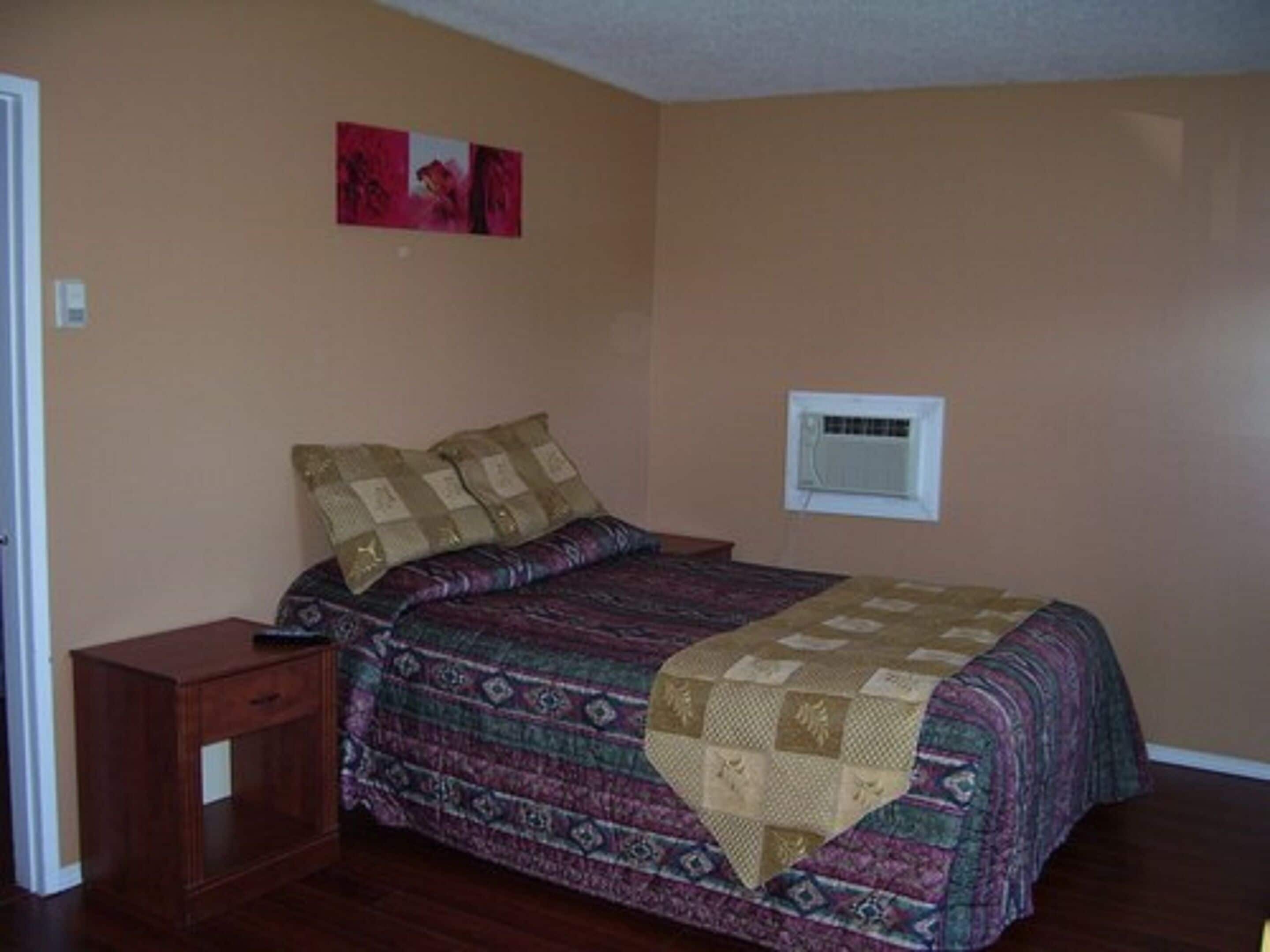 Un dormitorio con cama, mesita de noche, aire acondicionado de pared y una puerta.