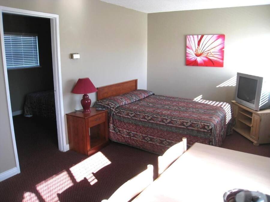A bedroom with a bed, a nightstand, a lamp, a TV, and a painting on the wall.