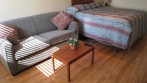 A room with a sofa, a bed with patterned bedding, a small table with a plant, and a lamp on a nightstand. - Beach Grove Motel (Delta)