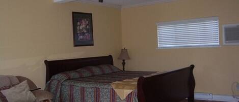 A bedroom with a bed, a chair, a lamp, and a window with blinds.